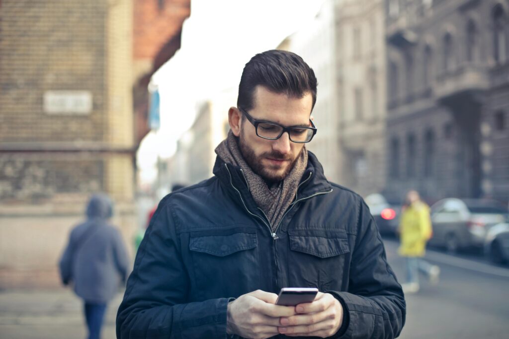 Adult man with glasses using a smartphone on a city street in Budapest, Hungary.